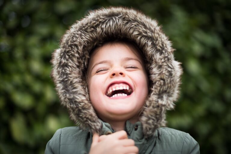 First orthodontic exam at Morejon + Andrews Orthodontics, young boy smiling with fur hood in the forest