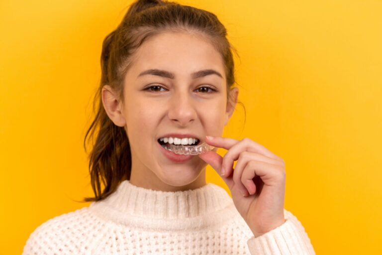 Young girl wearing turtle neck, holding Invisalign clear aligner in her mouth, after orthodontic treatment at Morejon + Andrews Orthodontics