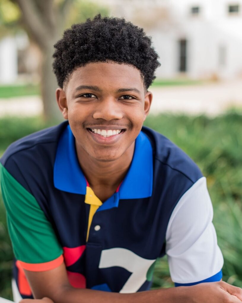 Young teen boy wearing colorful polo, smiling at camera with beautiful new smile from Morejon + Andrews Orthodontics orthodontic treatment
