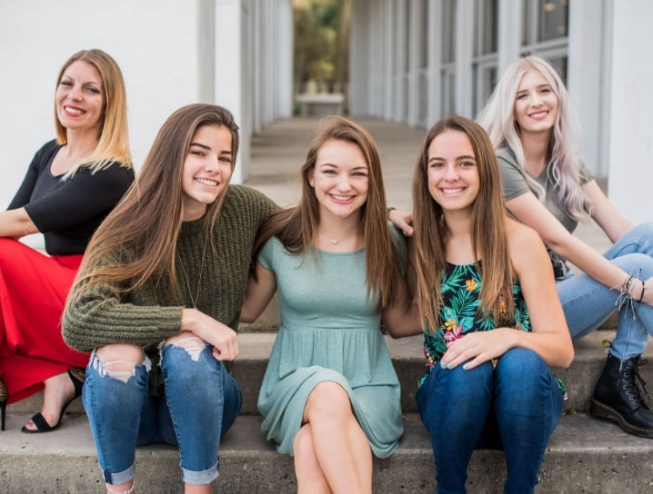 Five female patients at Morejon + Andrews Orthodontics sitting on steps at orthodontist office smiling at camera with beautiful new teeth