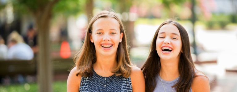 two teens show off their clean braces after learning the difference of waterpik vs flossing with braces