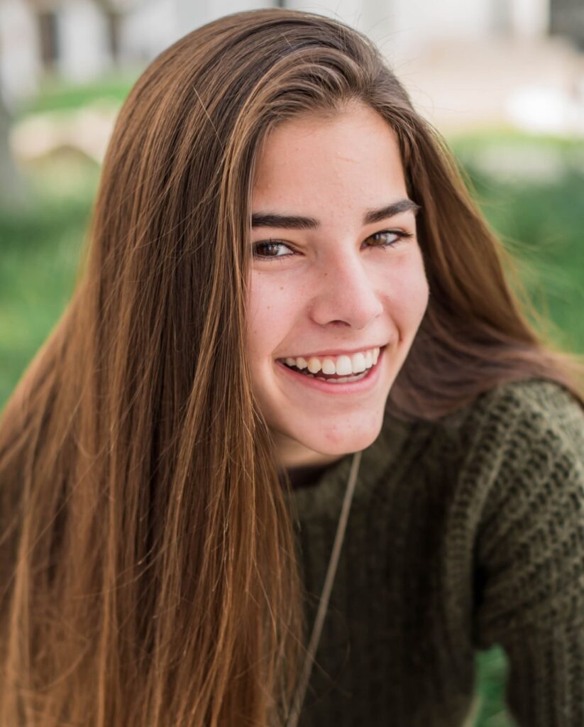 Young teen girl with brown hair smiling at camera with results from orthodontic treatment at Morejon + Andrews Orthodontics