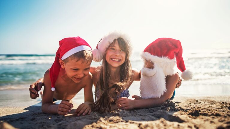 siblings lay on the beach wearing santa hats and talk about stocking stuffer ideas